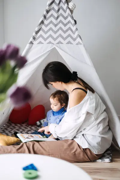 stock image A mother reads to her toddler inside an indoor tent, showcasing a thoughtfully designed play space that encourages engaging and child-friendly home activities.