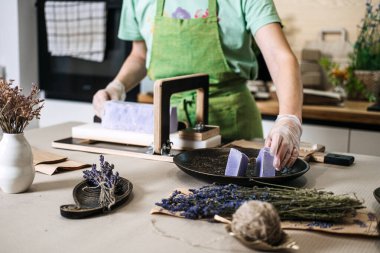 El yapımı lavanta sabununu tel kesiciyle doğrayan ellerin yakın çekimi. Sanata, organik cilt bakımına ve doğal kozmetik üretimine odaklan..