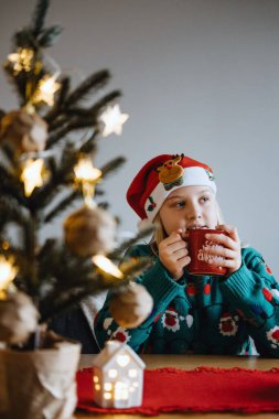 Noel kıyafetli genç kız sıcak bir içkinin keyfini çıkarıyor, Noel ruhunu ve mevsimlik neşesini yakalıyor..