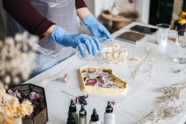 Çiçekleri DIY ev dekorasyonu için bir reçine çerçevesine yerleştirerek geleneksel el sanatları ve sürdürülebilir çevre dostu teknikleri vurgulayan ellerin yakın plan çekimi.