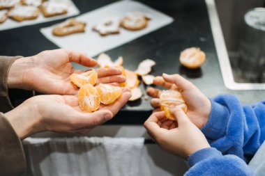 Anne ve kızı basit bir anın tadını çıkarıyorlar. Mutfakta portakal soyuyorlar, Noel neşesinin, kaliteli zamanın ve tatil mutluluğunun özünü yakalıyorlar..