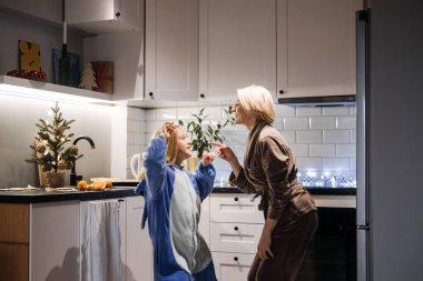 Anne ve kız mutfakta neşeyle dans ediyor, Noel birlikteliğinin, tatil ruhunun ve paylaşılan aile deneyimlerinin neşesini yakalıyorlar..