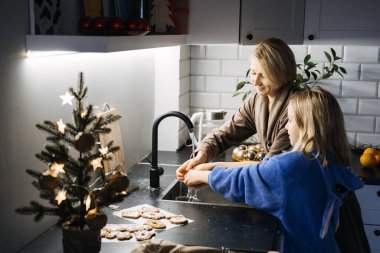 Mother and daughter sharing joyful moments while baking Christmas treats in a festive kitchen on Christmas Eve, celebrating family bonding and holiday traditions. clipart