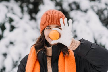 Kışın açık havada elinde portakal tutan neşeli bir kadın. Neşeli kış yaşam tarzı ve mevsimsel tazelik kavramı