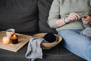 Person knitting on a cozy couch with candles, representing the slow living trend, mindfulness, and creative self-care practices clipart