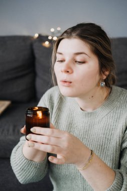 Elinde mum tutan bir kadın, sıcak ortam aydınlatmasıyla rahat bir atmosfer yaratıyor. Hygge yaşam tarzını ve huzurlu ev atmosferini kucaklamak