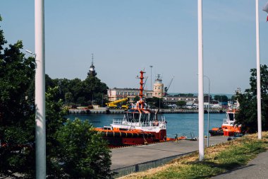 Orange tugboats docked at a waterfront near historic lighthouse and maritime buildings. Gdansk port scene. Gdansk, Poland - May 19, 2024. clipart