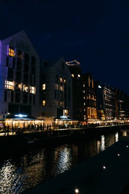 Motlawa Nehri 'ndeki modern aydınlık binaların ve yansımalarının gece vakti liman manzarası. Gdansk, Polonya - 19 Mayıs 2024.
