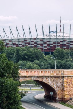 PGE Narodowy Stadyumu tarihi taş köprünün ve yemyeşil çimlerin arkasında. Varşova, Polonya, 19 Mayıs 2024.
