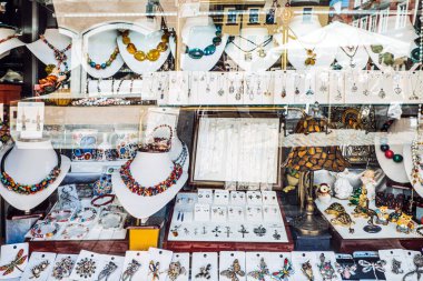 Kolyeler, küpeler, broşlar, dekoratif parçalar sergilenen sanatsal tasarımlar ve karmaşık detaylarla dolu canlı bir kuyumcu penceresi.