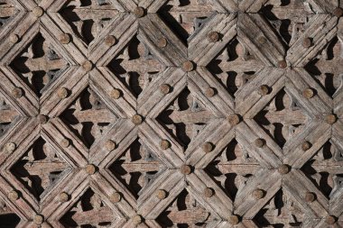 Geometrik tasarımlar ve yıpranmış dokular içeren eski ahşap kafes deseninin ayrıntılı görünümü, sanatsal işçiliğin ve tarihsel mimari detayların vurgulanması
