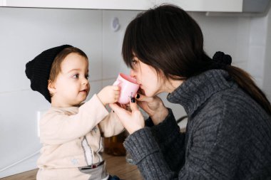 Anne, bebeğe bardaktan içmesi için yardım ediyor, duygusal güvenliğin sağlanmasındaki rahatlık ve rutinin rolünü vurguluyor ve sağlıklı erken çocukluk alışkanlıkları kuruyor..