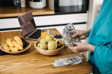 Woman budgeting money while preparing fresh meals in a cozy kitchen. Budgeting for healthy living, mindful spending, and cost-effective nutrition clipart