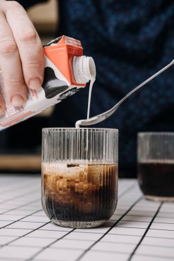 Bir bardakta buzlu kahveye süt dökmek. Ev kahvecisi konsepti, asgari masa üstü estetiği, içecek hazırlama