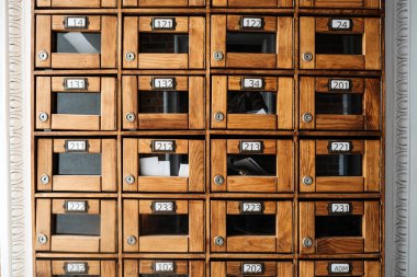 Numarası cam-önlü kompartımanları olan klasik ahşap posta kutusu duvarı analog iletişimi ve mimari nostaljiyi sembolize ediyor. Retro tasarım, analog canlanma, organizasyonel sistemler