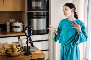 Ev mutfağında yüzük lambası ve dizüstü bilgisayarla yaşayan genç bir kadın. Yaratıcı ekonomi, dijital orijinallik ve solo girişimcilik eğilimlerini araştırır.