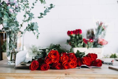 Çiçekçi stüdyosunda, vazoda okaliptüs ile paketlenmeye hazır kırmızı gül buketi. Aylık çiçek aboneliklerini ve romantik hediye törenlerini yansıtıyor.