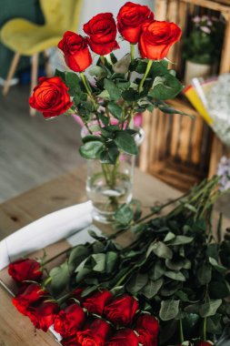 Çiçekçilerin masasında düzenlenmesi için daha fazla kökü olan temiz bir vazoda sergilenen taze kırmızı güller. Romantik gösteri, çiçek stili, çiçek dekoru, çiçekçi ambiyansı, aşk dili.. 