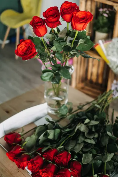 Çiçekçilerin masasında düzenlenmesi için daha fazla kökü olan temiz bir vazoda sergilenen taze kırmızı güller. Romantik gösteri, çiçek stili, çiçek dekoru, çiçekçi ambiyansı, aşk dili.. 