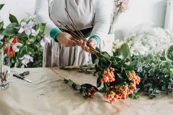 Çiçekçi dikkatlice portakal meyveleri ve karışık yeşillik ile elle bağlanmış bir buket hazırlıyor. Yavaş çiçekçilik, dikkatli üretim, zanaatkar çiçek tasarımı, çiçek sağlığı, doğadan esinlenilmiş iş.. 