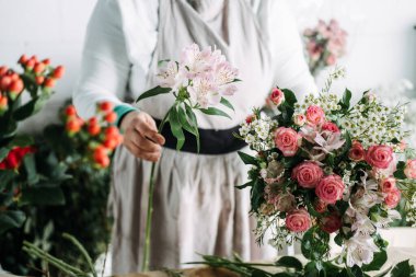 Çiçekçi, stüdyo çiçekleri kursunda pembe güller ve böğürtlenler kullanarak buket yaptığını gösteriyor. Çiçek eğitimi ve zanaat dersleri, pratik beceriler, yaratıcı öğrenme, buket yapma. 