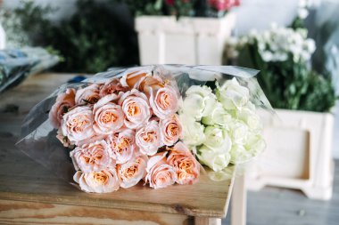 Çiçek stüdyosundaki ahşap bir masada duran şeftali buketleri ve beyaz güller. Çiçek atölyesi, çiçek düzenleme sınıfı, çağdaş çiçekçilik, buket hazırlığı. Yüksek kalite fotoğraf