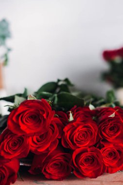 Ahşap bir masanın üzerine yerleştirilmiş yemyeşil bir gül buketinin yakın çekimi. Kırmızı güller, basit romantizm, zarif buketler, lüks hediyeler, ebedi güzellik, aşk sembolizmi. Yüksek kalite fotoğraf