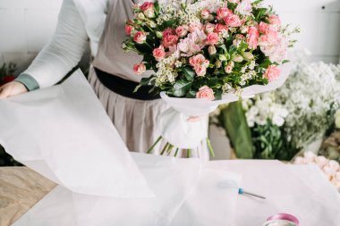 Çiçekçi, kıtır kıtır beyaz kağıda sarılmış karışık pembe çiçekleri sunar. Buket sunumu, çiçek ambalajı, eko çiçekçi, yerel çiçek işi. Yüksek kalite fotoğraf