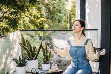 Bir kadın, şehir bahçesindeki saksılarda kollarını kaldırmış, balkonda meditasyon yapıyor. Balkon bahçıvanlığı, şehirde doğa, bitki terapisi, dikkatli anlar. Yüksek kalite fotoğraf