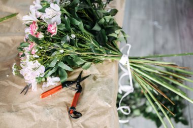 Çiçekçi çalışma alanı, yeni bağlanmış pembe çiçek buketi, makas ve kraft kağıdına budanmış saplar. Çiçekçi çalışma alanı, buket hazırlığı, yavaş çiçek hareketi, çiçekçilik.. 