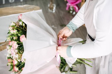 Çiçekçi pembe güller ve alstromerya buketinin etrafına pembe saten bir kurdele bağlıyor. Buket sunumu, çiçek ambalajı, esnaf hediyesi, sürdürülebilir ambalaj. Yüksek kalite fotoğraf