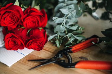 Kırmızı güller, okaliptüs ve çiçekçilerin kullandığı ahşap makaslar. Çiçek düzenleme, pratik yaratıcılık, gül buketi, zanaatkar çiçekçi, çalışma süreci. Yüksek kalite fotoğraf