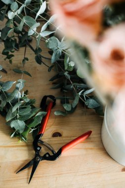 Kırmızı güller, okaliptüs ve çiçekçilerin kullandığı ahşap makaslar. Çiçek düzenleme, pratik yaratıcılık, gül buketi, zanaatkar çiçekçi, çalışma süreci. Yüksek kalite fotoğraf