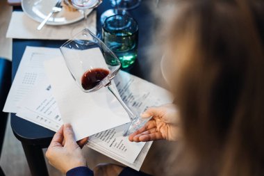 Restaurant masasına basılmış tadımlık notların üzerine eğilmiş bir bardak kırmızı şarap. Şarap tatma, duyusal deneyim, kasıtlı yemek, kişisel zenginleştirme. Yüksek kalite fotoğraf