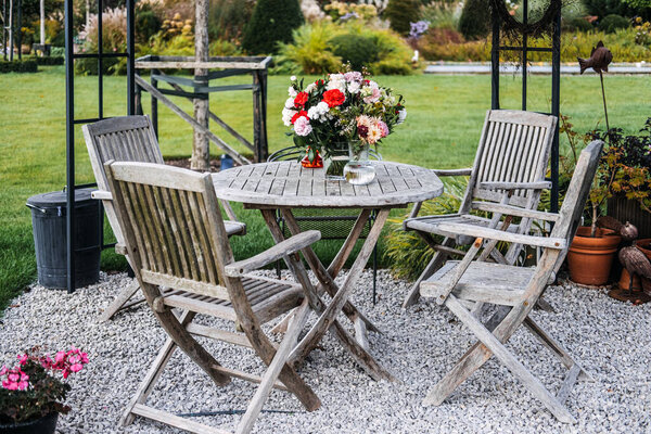 Выветриваемая деревянная садовая мебель со свежим букетом цветов в саду. Уличная жизнь, ржавый дизайн, устойчивые материалы, медленный образ жизни. Высокое качество фото
