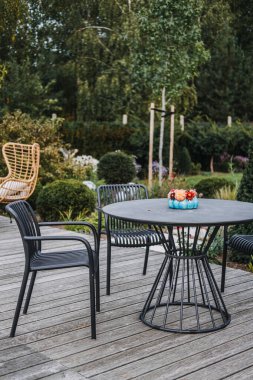 Çağdaş siyah teras mobilyaları, yemyeşil bir bahçedeki ahşap bir güvertede küçük bir çiçek aranjmanı. Çağdaş açık hava yaşamı, minimalist bahçe tasarımı, çevre bilinci olan ev dekorasyonu, mevsimlik çiçekler.. 