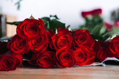 Çiçekçi stüdyosunda, vazoda okaliptüs ile paketlenmeye hazır kırmızı gül buketi. Aylık çiçek aboneliklerini ve romantik hediye törenlerini yansıtıyor.