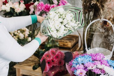 Çiçekçi, diğer renkli düzenlemelerin yanında çizgili kağıda sarılı bir buket beyaz çiçek sunuyor. Sanatsal buketler, özel çiçek düzenlemeleri, modern çiçekçiler, yaratıcı hediyeler.. 
