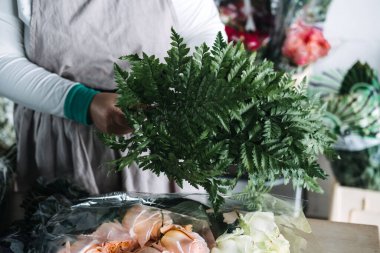 Çiçekçilik, çiçeklerle dolu bir stüdyoda çalışma masasında taze yeşillik ve güller düzenliyor. Modern çiçekçi atölyeleri, çiçekçilik eğitimi, aktif buket tasarımı, botanik işçiliği.. 