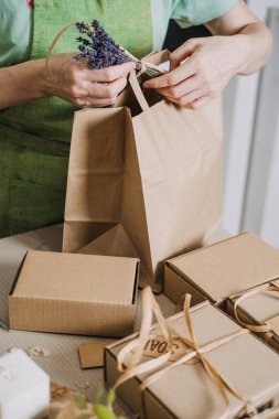 Küçük bir işletme sahibi, hediye kutularıyla çevrili kahverengi bir kesekağıdına aşk etiketi ve lavanta filizi ile el yapımı bir el işi bağlıyor. Ev yapımı iş, el yapımı mallar. Yüksek kalite fotoğraf