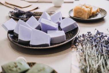 Yanında kurutulmuş lavanta ve yeşil sabunla seramik bir tabağa dizilmiş el yapımı lavanta sabunları yakın plan. Aromaterapi, temiz güzellik, sürdürülebilir malzemeler, botanik cilt bakımı. kalite fotoğraf