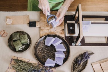 Şifalı otlar ve ambalaj malzemeleriyle çevrili el yapımı lavanta sabunlarını rafine eden bir kadının en iyi görüntüsü. Botanik sağlık, bitkisel cilt bakımı, temel yağlar, sakinleştirici aromaterapi. Yüksek kalite fotoğraf
