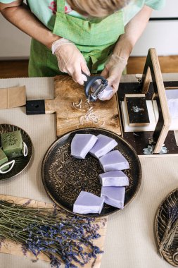 Şifalı otlar ve ambalaj malzemeleriyle çevrili el yapımı lavanta sabunlarını rafine eden bir kadının en iyi görüntüsü. Botanik sağlık, bitkisel cilt bakımı, temel yağlar, sakinleştirici aromaterapi. Yüksek kalite fotoğraf