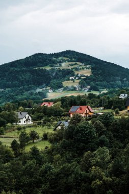 Orman ve tarım yamaçlarının arasında dağınık evleri olan bir dağ köyü manzarası. Çevre turizmi, sürdürülebilir turizm, kültürel koruma, otantik köy deneyimleri..