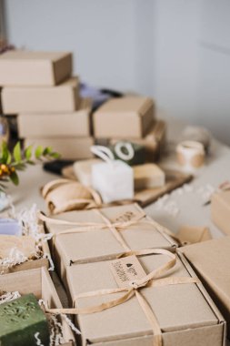 El yapımı sabunlar ve doğal dolgular içeren Kraft Spa hediye kutularıyla dolu bir masa. Spa hediye kutusu, el yapımı sağlık ürünleri, sakinleştirici ritüeller, stres atma hediyeleri. Yüksek kalite fotoğraf