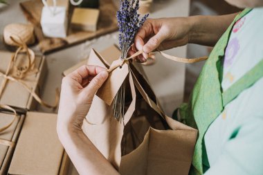 Kraft hediye paketini lavanta ve kurdeleyle doğal ambalaj setiyle bağlayan eller. Çevre dostu markalar, sürdürülebilir ambalajlar, plastiksiz, sıfır atık ambalajı. Yüksek kalite fotoğraf