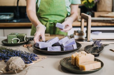 Kişi, diğer el yapımı sabunlar ve kurutulmuş çiçeklerin yanında taze yapılmış lavanta sabunlarını bir tabağa koyar. Sanatsal küçük işletme, düşük atık ambalajlama, sağlıklı yaşam tarzı. Yüksek kalite fotoğraf