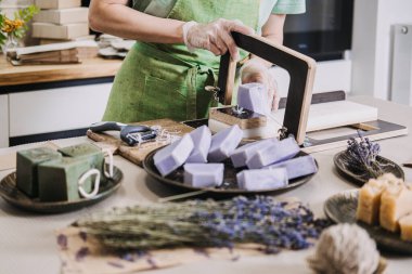 Mutfak masasında sabun makası ve kurutulmuş çiçeklerle hazırlanmış el yapımı lavanta sabunları. Temalar arasında doğal cilt bakımı ürünleri, aromaterapi, sıfır atık güzellik yer alıyor. Yüksek kalite fotoğraf