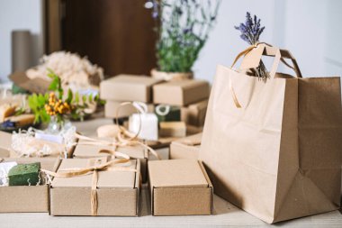 Doğal sabun hediye kutuları ve kraft çantaları çiçek desenli bir masada düzenlenir. El yapımı hediyeler, tatil hazırlığı, doğal cilt bakımı hediyesi, sağlık hediyesi kutusu. Yüksek kalite fotoğraf