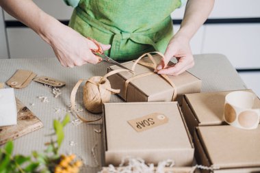 Kurdeleli kraft kutuları hazırlıyor. Üzerinde sabun etiketi asgari zanaatkar çalışma alanında. Gen Z alışveriş alışkanlıkları, anlamlı tüketim, üretim kültürü, kişisel eşyalar. Yüksek kalite fotoğraf